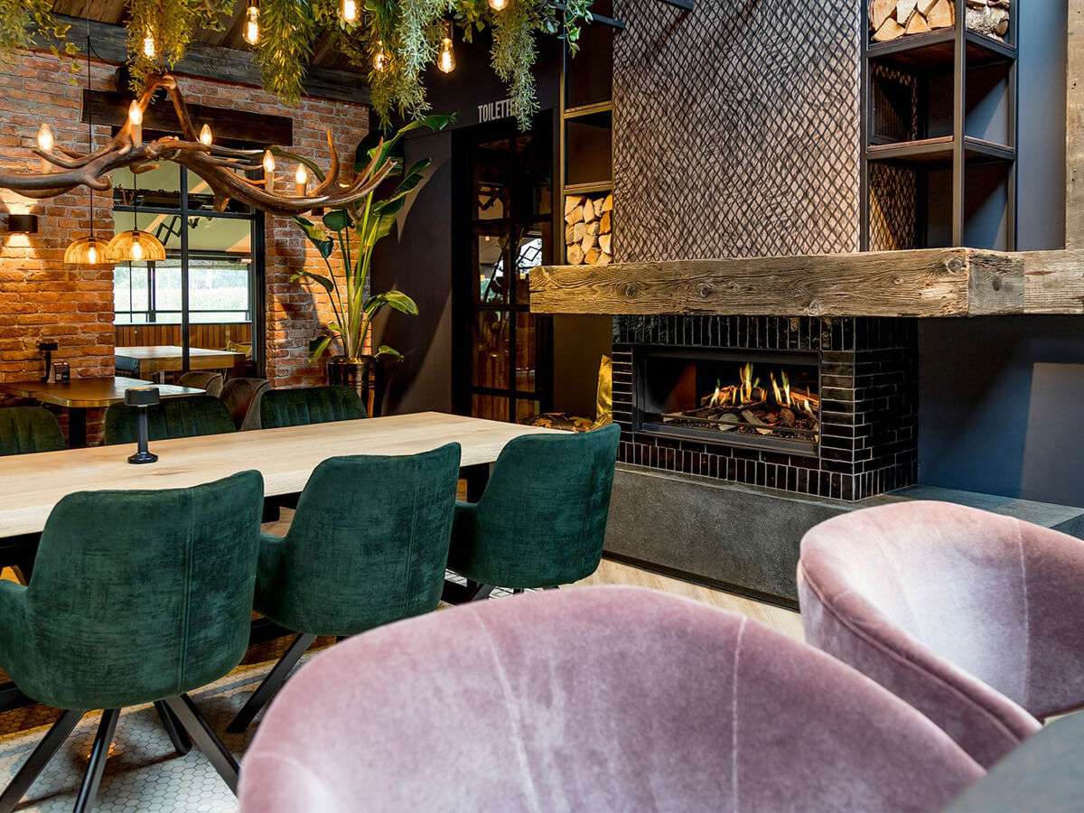 NetZero Fire E-One 130F 3D Electric Fireplace - Front - AA-11-05387 installed in a chic dining space with velvet chairs, wood accents, and lush greenery.