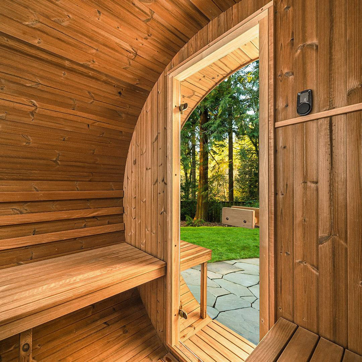 Interior doorway view of Thermory Barrel Sauna Model #60 DIY Kit with wood benches and outdoor garden scene. Inviting home spa solution.
