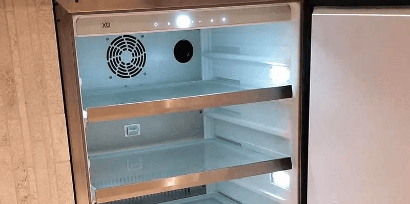 XO 15 Inch Outdoor Undercounter Refrigerator open with empty glass shelves and interior LED lights, highlighting spacious storage design.