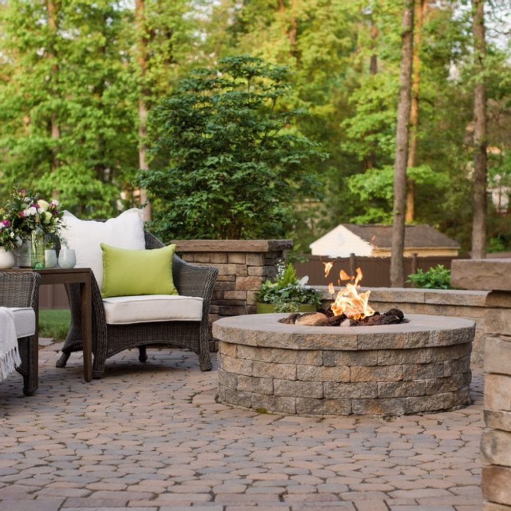 Installed Firegear DIY Fire Pit Kit - Round in a stone patio setting with wicker furniture, ideal for cozy outdoor gatherings.