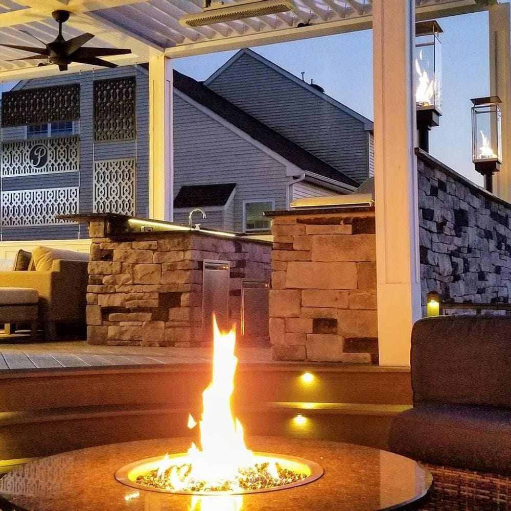 Evening patio scene with Firegear DIY Fire Pit Kit - Round lit up, surrounded by stone walls and ambient lighting.