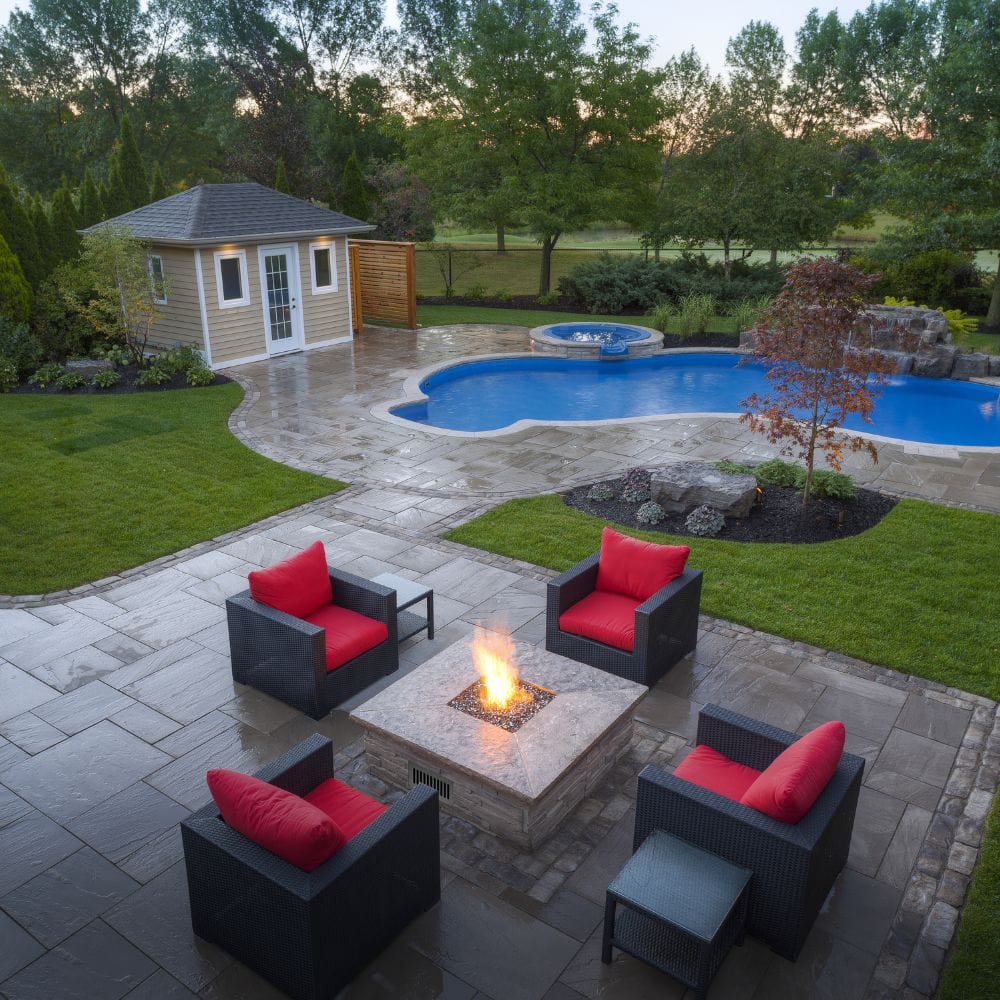 Spacious backyard with pool and Firegear DIY Fire Pit Kit - Square installed in a stone fire pit, offering warmth and style.