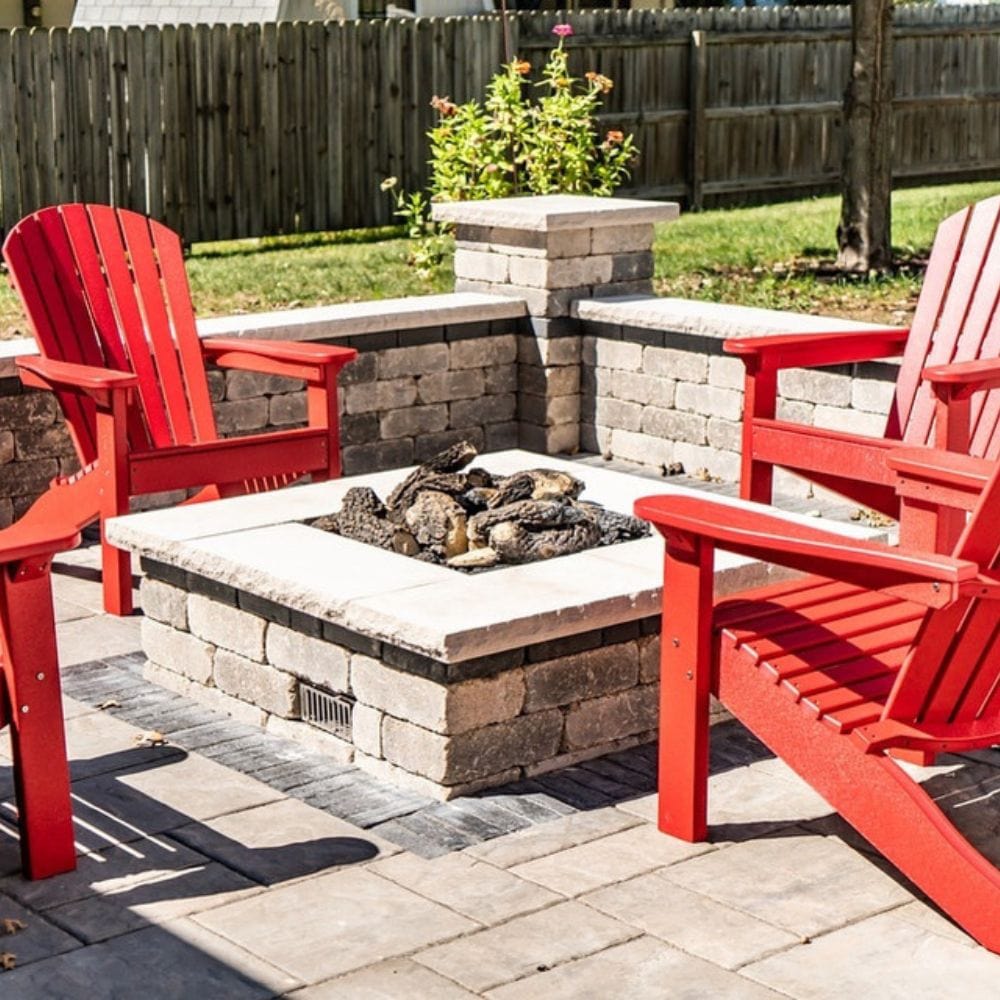Patio with red Adirondack chairs surrounding a Firegear DIY Fire Pit Kit - Square installed in a stone base with natural gas flames.