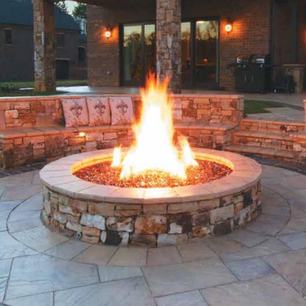 Firegear Burning Spur installed in a round stone fire pit, producing a large flame in a luxurious outdoor patio seating area.