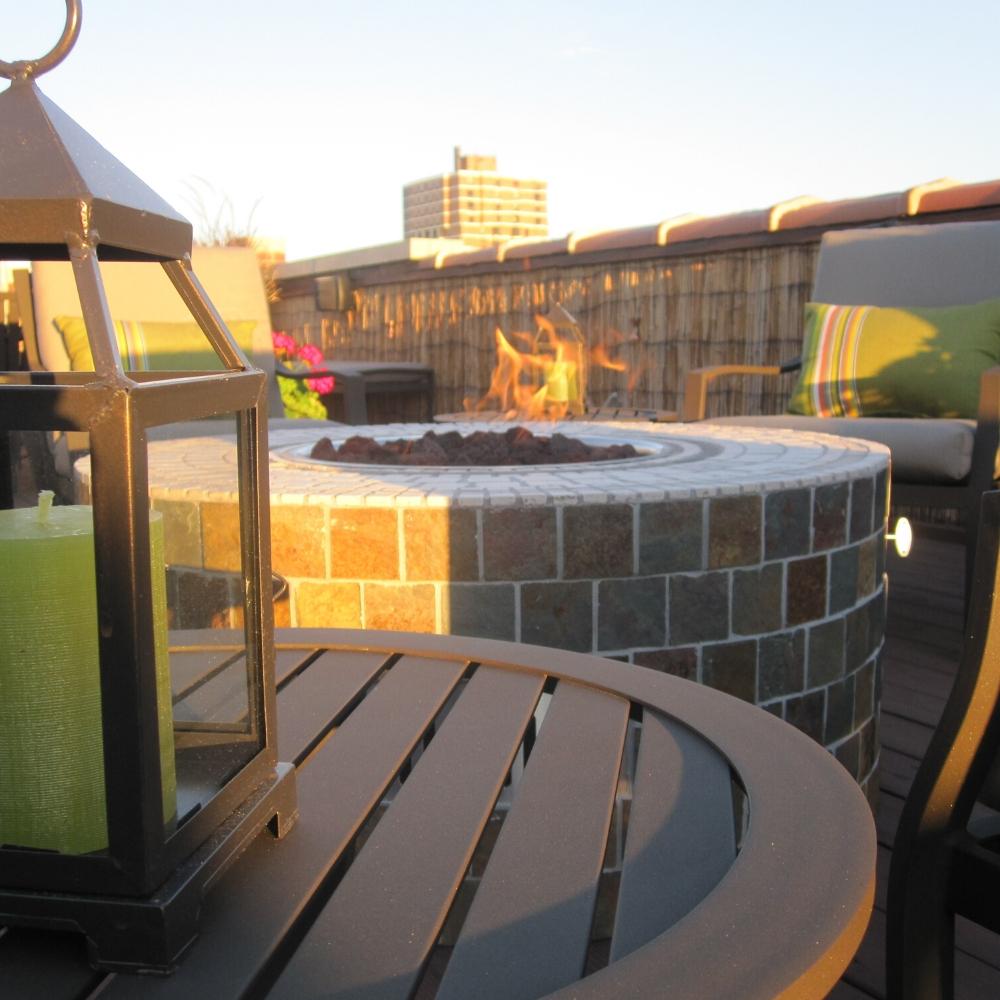 Close-up of tiled Firegear DIY Fire Pit Kit - Round on rooftop deck, paired with modern patio furniture and lantern decor.