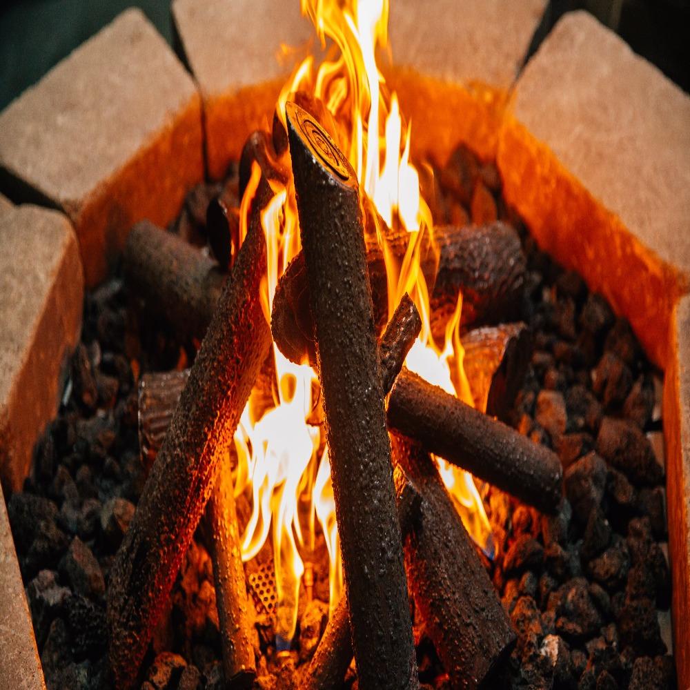 Close-up of Firegear Pro Series brass gas burner flames with realistic ceramic logs and lava rocks in a fire pit setup.