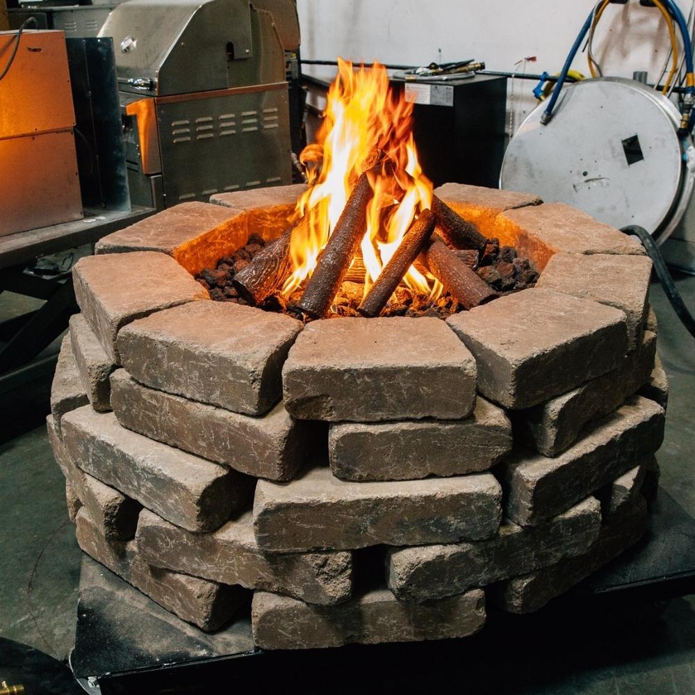 Outdoor fire pit with Firegear Pro Series Burning Spur brass burner in action, surrounded by stacked stone and producing tall flames.