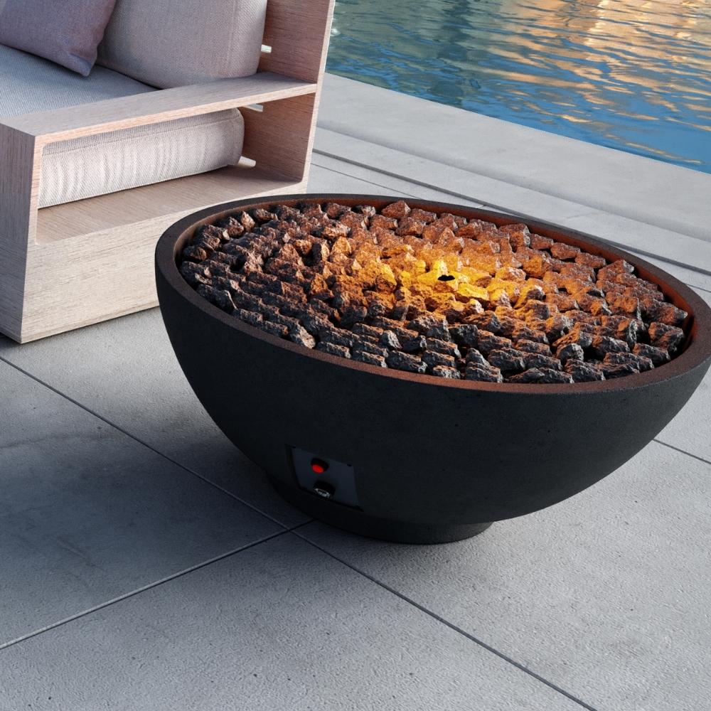 Firegear Sanctuary 39-Inch Round Concrete Gas Fire Bowl in Raven finish lit with lava rocks, creating a cozy poolside ambiance.