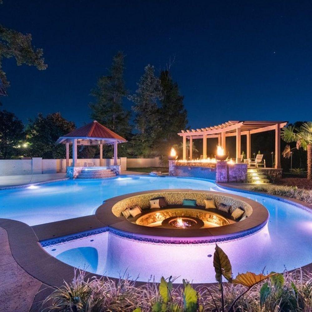 Night view of illuminated pool and Firegear Sanctuary 30-Inch Round Concrete Gas Fire Bowl in cozy sunken lounge area.