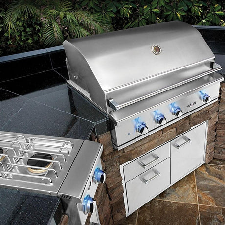 Delta Heat 32 inch built-in gas grill with blue lit knobs in a stone outdoor kitchen island with a side burner and storage drawers