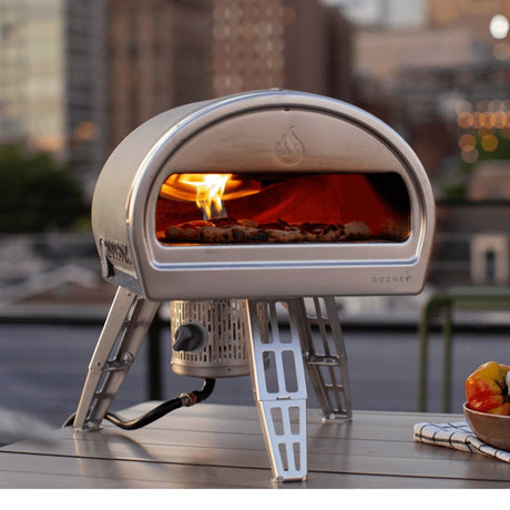 Gozney Roccbox portable pizza oven with a pizza baking inside, on an outdoor table with a city skyline behind