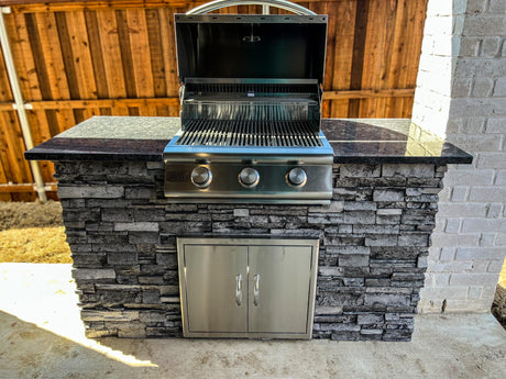 Built-in Blaze 25 inch gas grill with its hood open in a 5 foot stacked stone outdoor kitchen island with a dark granite countertop