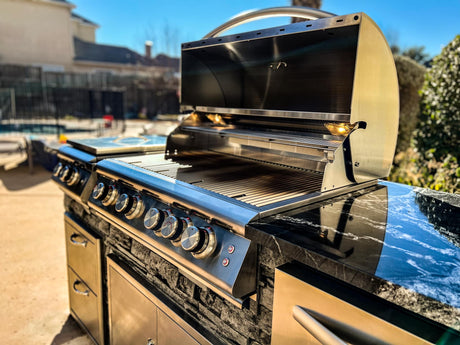 Blaze 32 inch gas grill with its hood open built into an 8 foot stacked stone outdoor kitchen island with a dark marble countertop