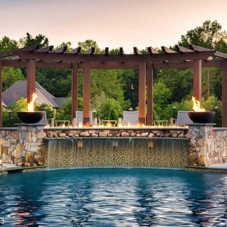 Firegear Sanctuary 30-Inch Round Concrete Gas Fire Bowls on stone pillars beside pool waterfall under wooden pergola.
